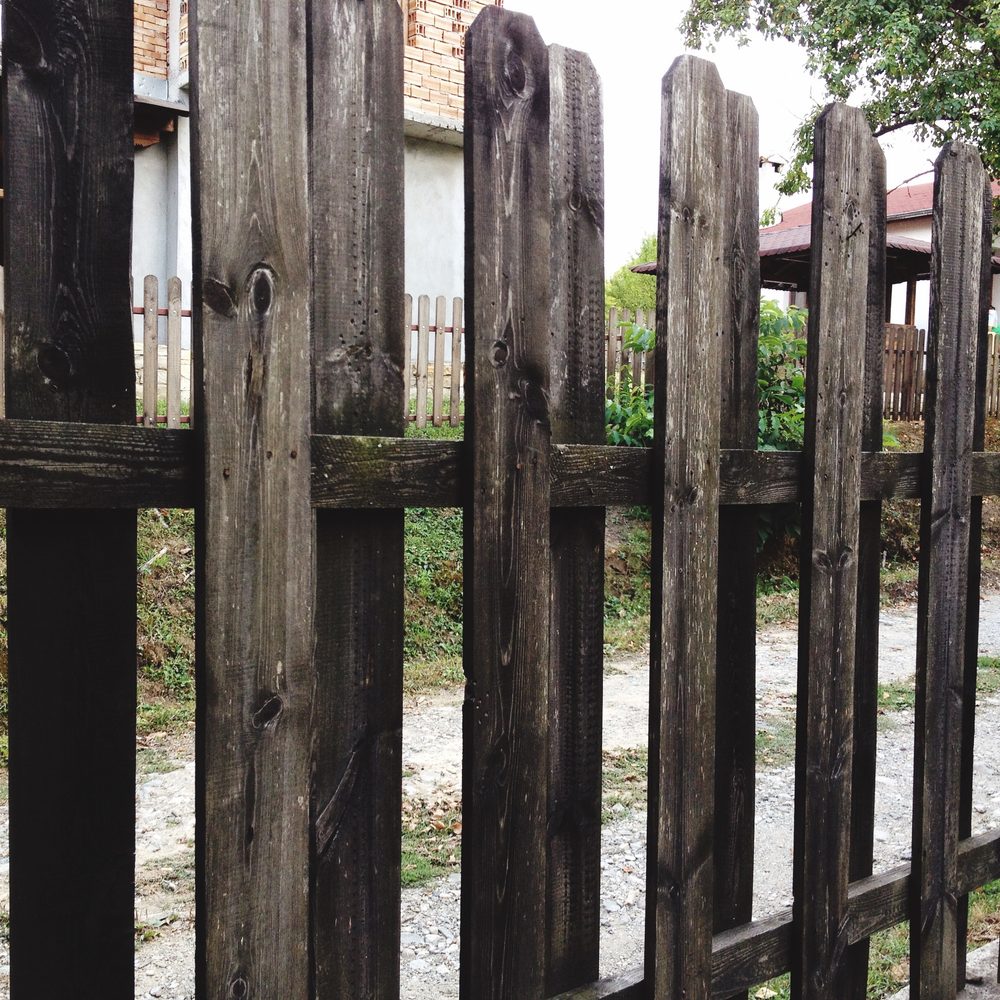Riparazione di una recinzione in legno deteriorata, con un nuovo palo accanto alla parte marcita.